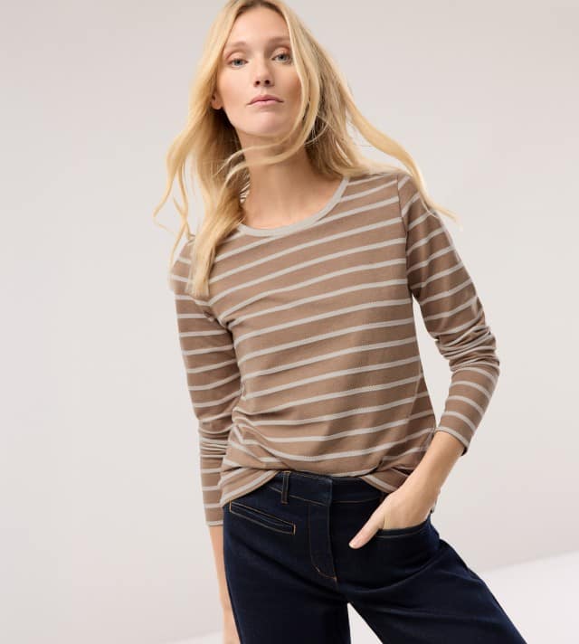 Eine Frau vor einem hellen Hintergrund trägt ein Baumwollshirt Ringelstruktur in Praline/Offwhite und dazu eine Marlene Jeans.