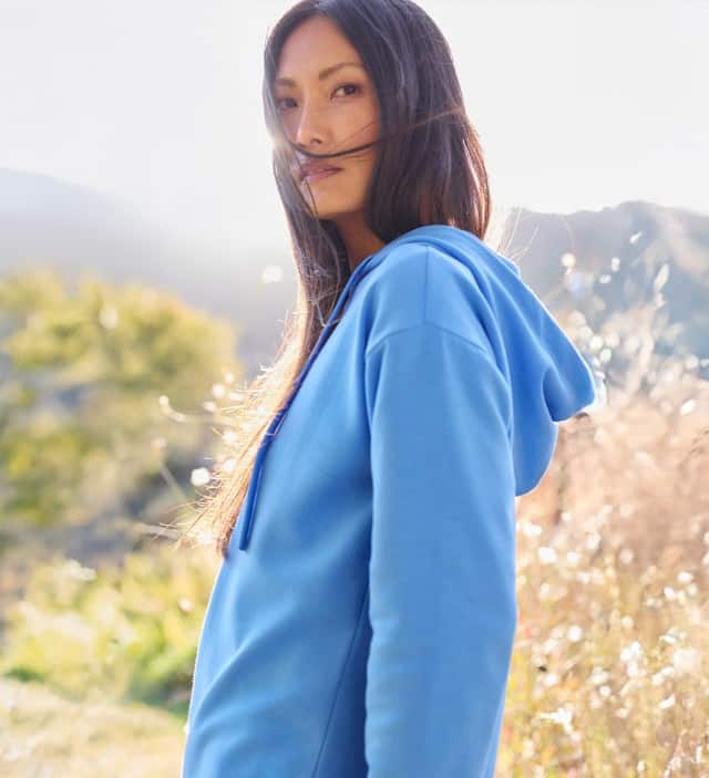 Eine Frau steht auf einem frühlingshaften Feld und trägt eine Hoodie in Blau.