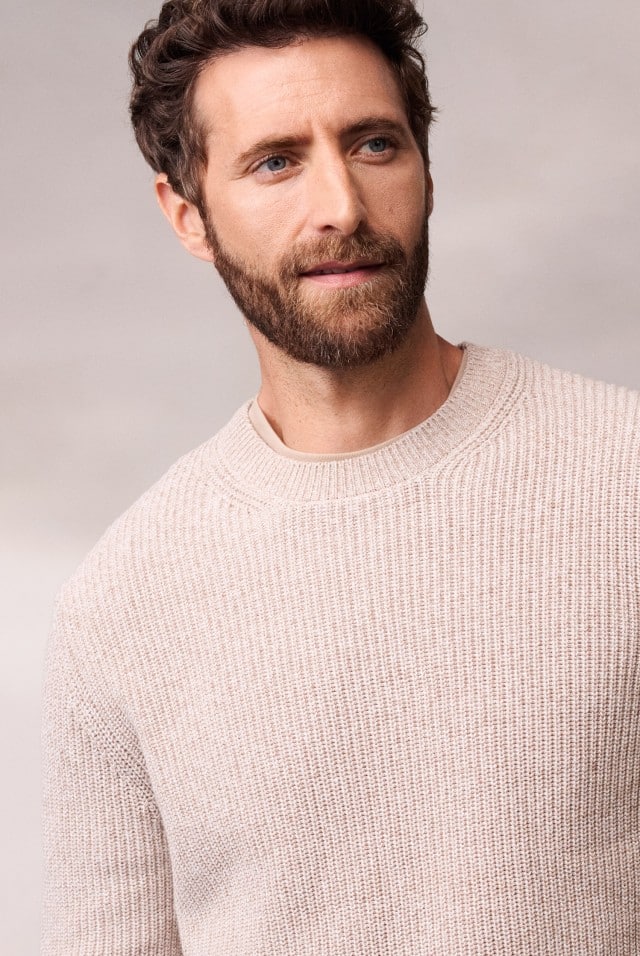 Ein Mann trägt einen hellen Strickpullover.