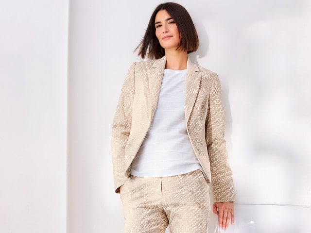 Eine Frau trägt einen Jacquardblazer in der Farbe Sand, darunter ein weißes Baumwollshirt mit Streifenstruktur und dazu eine passende Hose. Eine Frau trägt einen Jacquardblazer in der Farbe Sand, darunter ein weißes Baumwollshirt mit Streifenstruktur und dazu eine passende Hose.