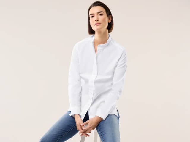 Eine Frau trägt eine weiße Bluse, dazu eine Jeans.