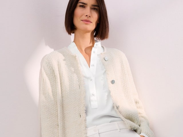 Eine Frau trägt eine weißt Bluse, darüber ein Cardigan in Creme und dazu die passende Hose.
