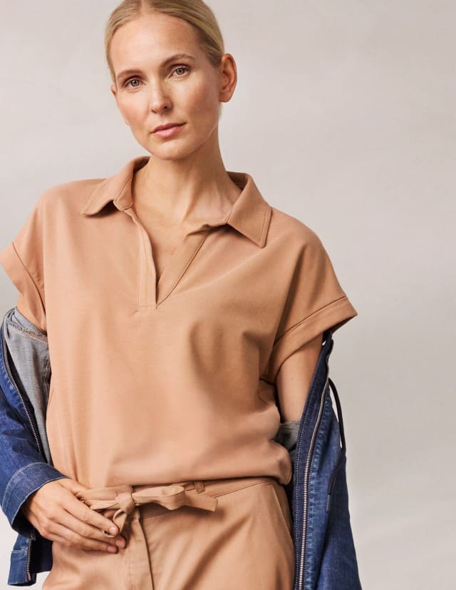 Eine Frau trägt ein Polo-Shirt in der Farbe Praline mit passender Hose und einer Leichtjacke aus Denim.