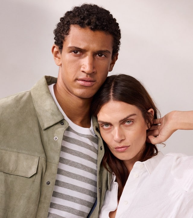 Ein Mann trägt eine Velourslederhemdjacke in Salbei mit passendem Shirt darunter und eine Frau in einer weißen Hemdbluse.