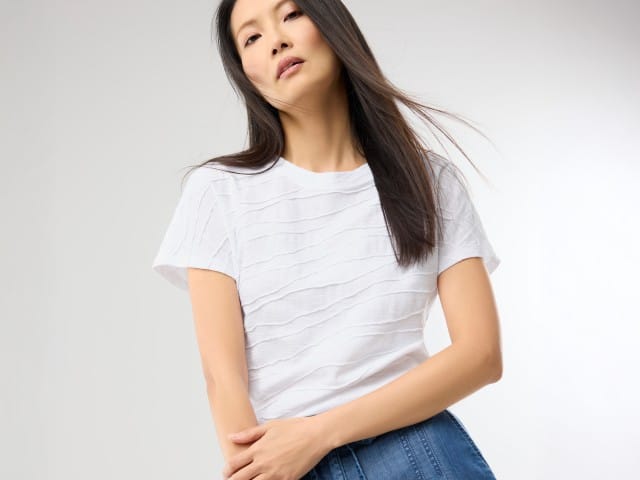 Person trägt ein weißes T-Shirt mit feiner, strukturierter Streifenoptik und eine blaue Jeans im modernen, schlichten Stil.