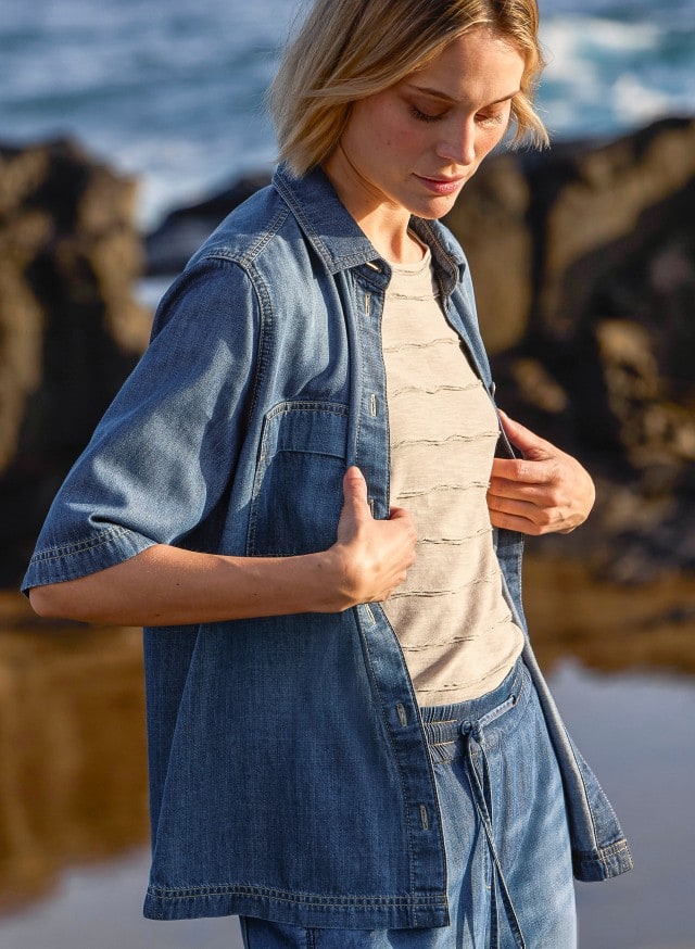 Eine Person trägt eine blaue Jeansbluse über einem hellen T-Shirt und dazu eine blaue Jeans – ein lässiger Freizeitlook.