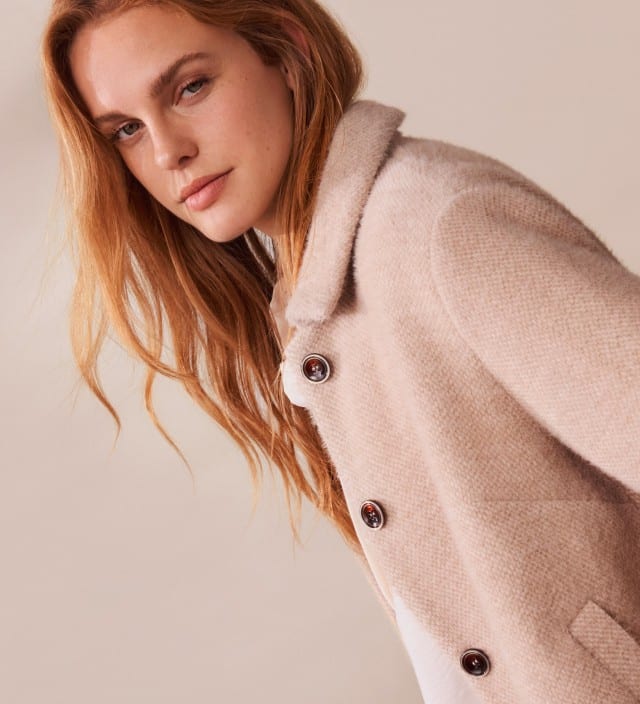 Ein Frau steht vor einem neutralen Hintergrund und trägt eine Kuscheljacke mit Kragen in Creme.