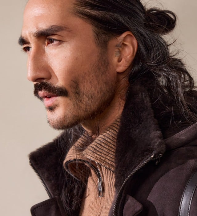 Seitenprofil eines Mannes, der einen hellen Pullover unter einer Kapuzenjacke trägt vor einem neutralen Hintergrund.