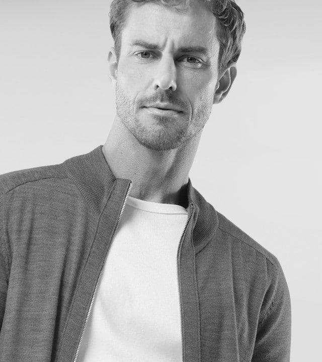 Ein Mann trägt einen Cardigan mit Reißverschluss, darunter ein weißes Shirt.