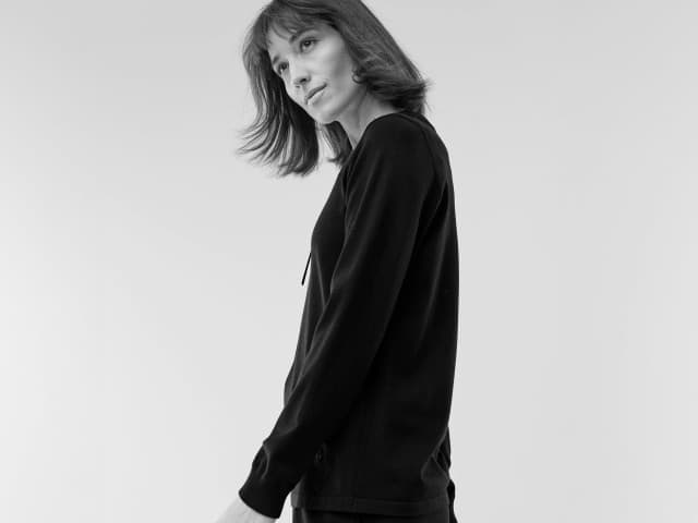 Eine Frau trägt einen schlichten, langärmeligen Pullover in dunkler Farbe, modern und minimalistisch gekleidet.