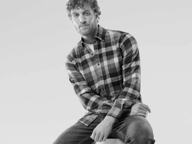 Ein Mann trägt ein kariertes Hemd und eine Jeans, lässig und modern gekleidet.