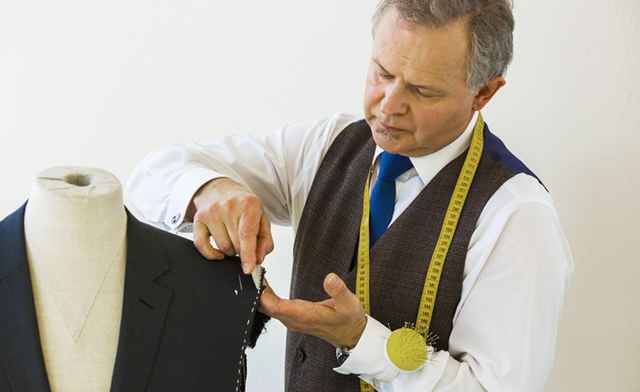 Schneider arbeitet an einer Anzugjacke auf einer Büste, mit Maßband um den Hals.