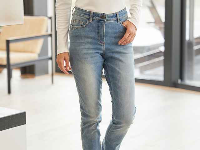 Frau trägt eine hellblaue Jeans und hat eine Hand in der Hosentasche.