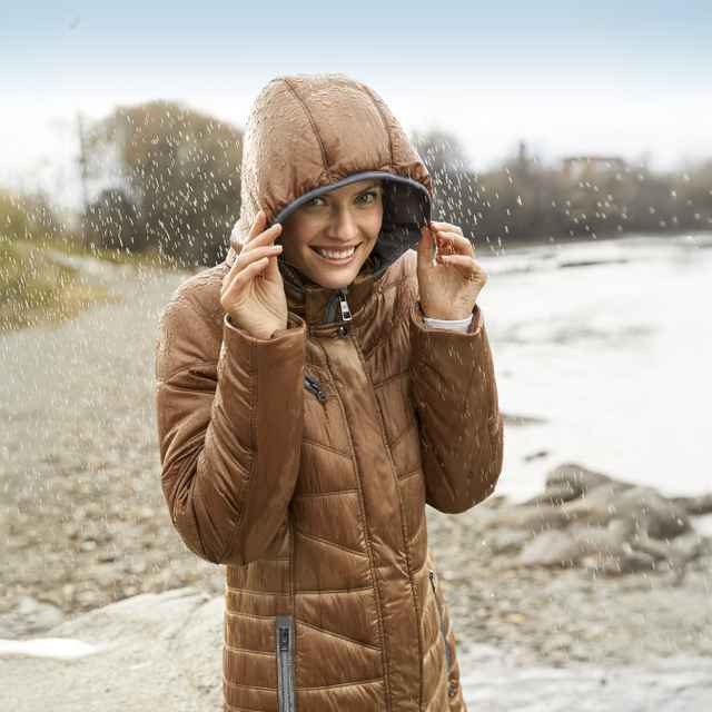 Frau steht in einer Wasserdichten Jacke im Regen und freut sich.