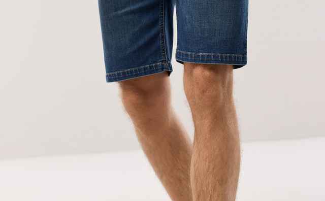 Ein Mann trägt eine dunkelblaue Jeans-Shorts, ein weißes T-Shirt und beigefarbene Espadrilles.