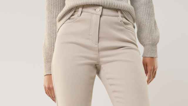 Eine Person trägt eine beigefarbene, figurbetonte Hose und einen hellgrauen Strickpullover. Der Stil wirkt schlicht, modern und elegant.
