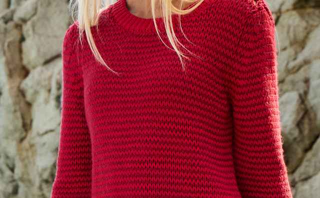 Eine Frau trägt einen Pullover mit dezentem Streifen in Signalrot.