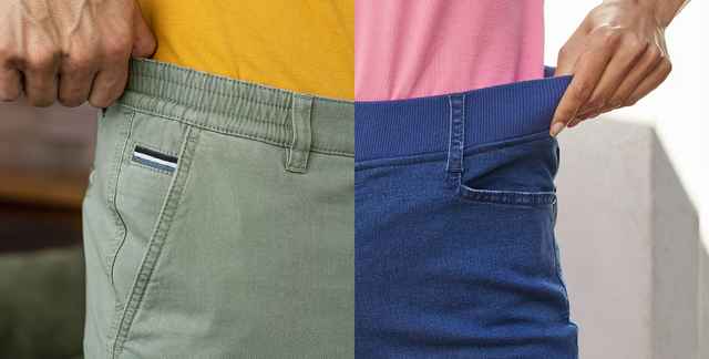 Zwei Personen ziehen an den Bund ihrer dehnbaren Hosen, links eine grüne Hose und rechts eine blaue Jeans.