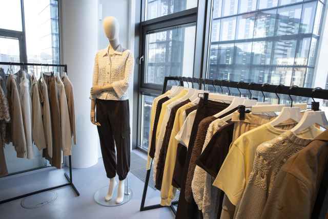 Schaufensterpuppe in eleganter Kleidung neben Kleiderständern mit beigefarbener und gelber Kleidung in einem modernen Geschäft.