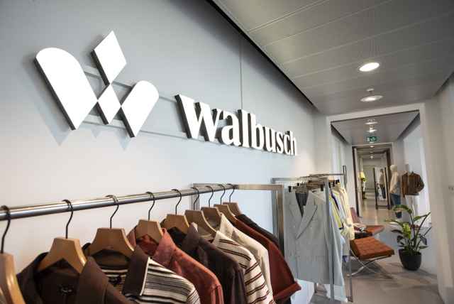 Kleiderständer mit Hemden und Jacken vor einem Wandlogo von Walbusch in einem Ladengeschäft.