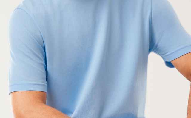 Mann mit grauem Bart in hellblauem T-Shirt und blauer Jeans sitzt entspannt auf einem weißen Hintergrund und schaut nach links.