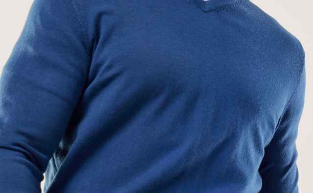 Mann in blauem Pullover und Jeans lächelt und blickt nach rechts vor einfarbigem Hintergrund.