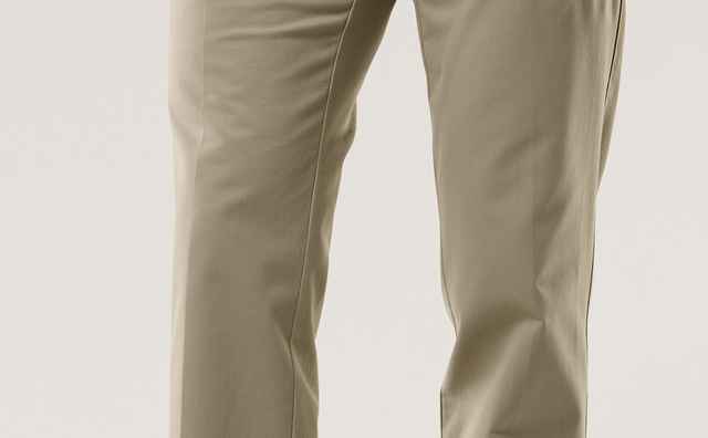 Mann trägt hellbraune Chinos mit einem schwarzen, gemusterten Gürtel, blauem Hemd und braunen Schuhen. Körper von der Hüfte abwärts gezeigt.