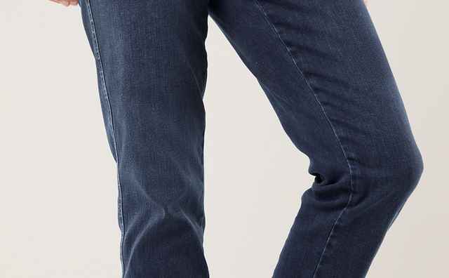 Person in dunkelblauer Jeans und grünem Shirt, trägt blaue Turnschuhe mit weißen Schnürsenkeln, posiert mit gebeugtem Bein.