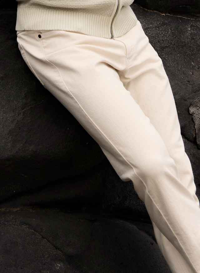 Person in cremefarbener Hose, lehnt an dunklem Felsen.
