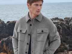 Ein Mann mit einer grauen Jacke steht vor Felsen und Meer, blickt nach links.