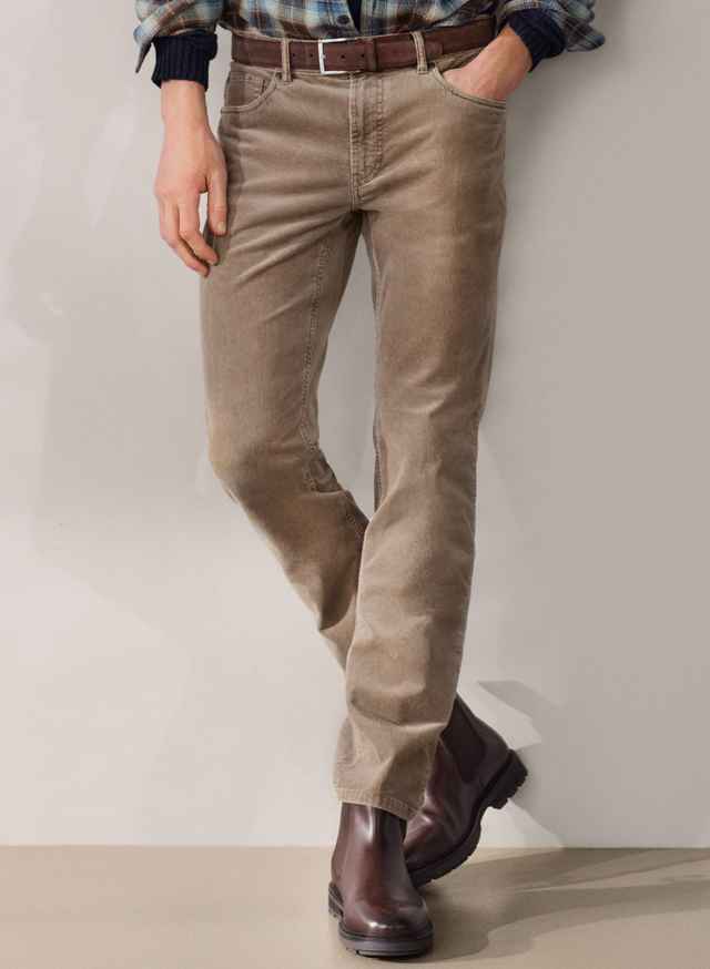 Person in beiger Cordhose mit braunem Gürtel und braunen Stiefeln, steht vor neutralem Hintergrund.