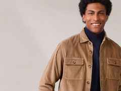 Mann in brauner Cordjacke und dunkelblauem Rollkragenpullover lächelt vor neutralem Hintergrund.