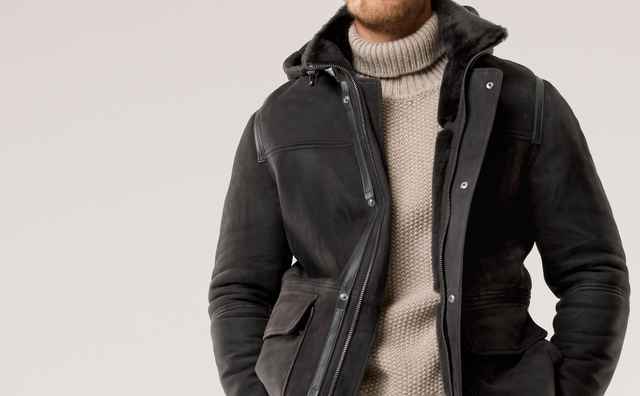 Mann in einer schwarzen, gefütterten Lederjacke  über einem beigefarbenen Rollkragenpullover und gemusterten Hosen – lässig-eleganter Winterstil.
