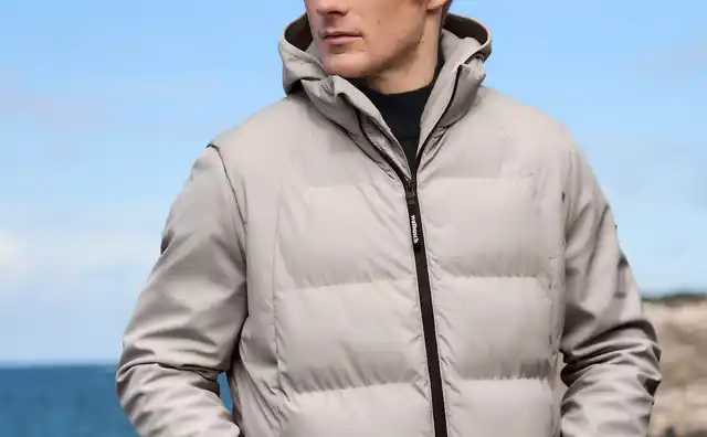 Mann in einer hellgrauen Outdoorjacke mit Kapuze, schwarzem Reißverschluss und sportlich-funktionalem Stil.