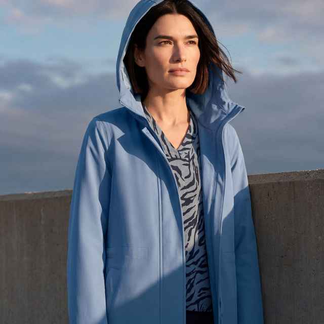 Person in einem hellblauen, funktionalen Jacke mit Kapuze über einem gemusterten Oberteil. Der Stil wirkt sportlich und modern.