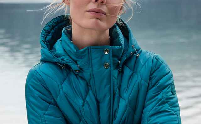 Person in einer türkisblauen, wattierten Steppjacke mit hohem Kragen und Kapuze. Der Stil wirkt sportlich und wetterfest.