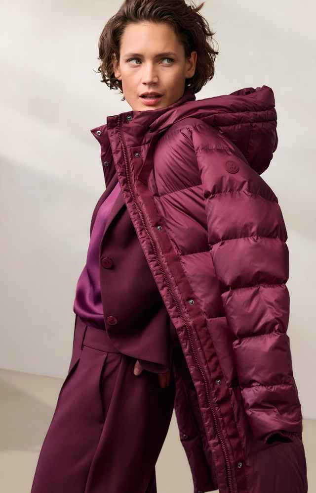 Eine Person trägt eine voluminöse, burgunderrote Winterjacke über einem passenden Anzug, lässig und modisch posierend.